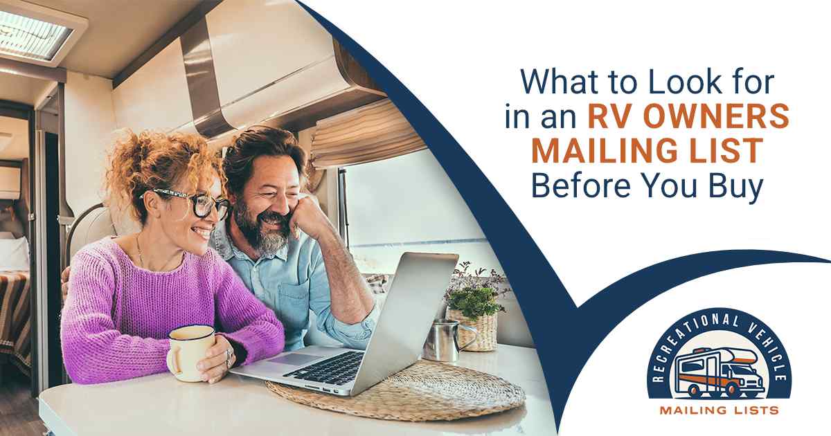 A smiling couple sitting at a table inside an RV, looking at a laptop together over coffee