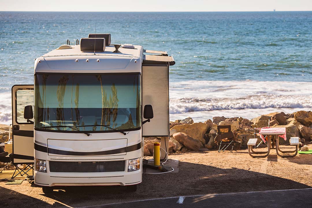 Class A motorhome parked at an oceanfront campsite with camp chairs beside the ocean