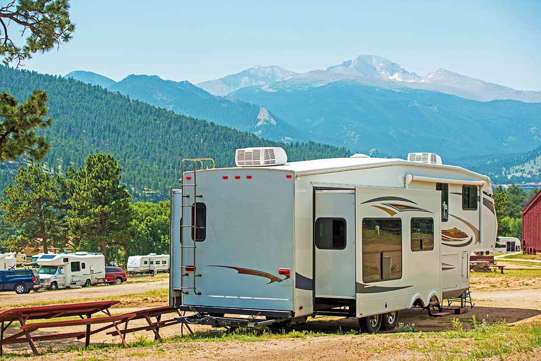 fifth wheel RV trailer parked at a mountain campground with pine trees and peaks