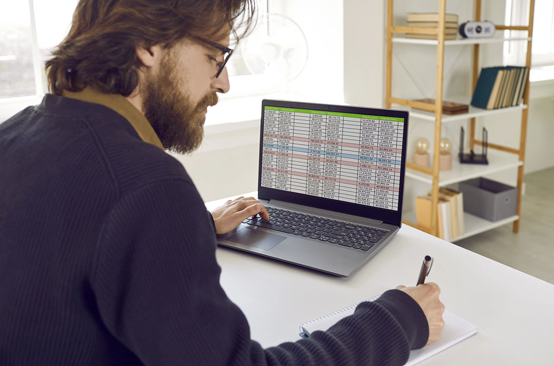 marketer at desk reviewing spreadsheet data on laptop with pen and notepad